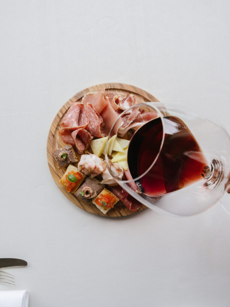 Vista dall'alto di un tagliere misto di affettati e formaggi con calice di vino rosso