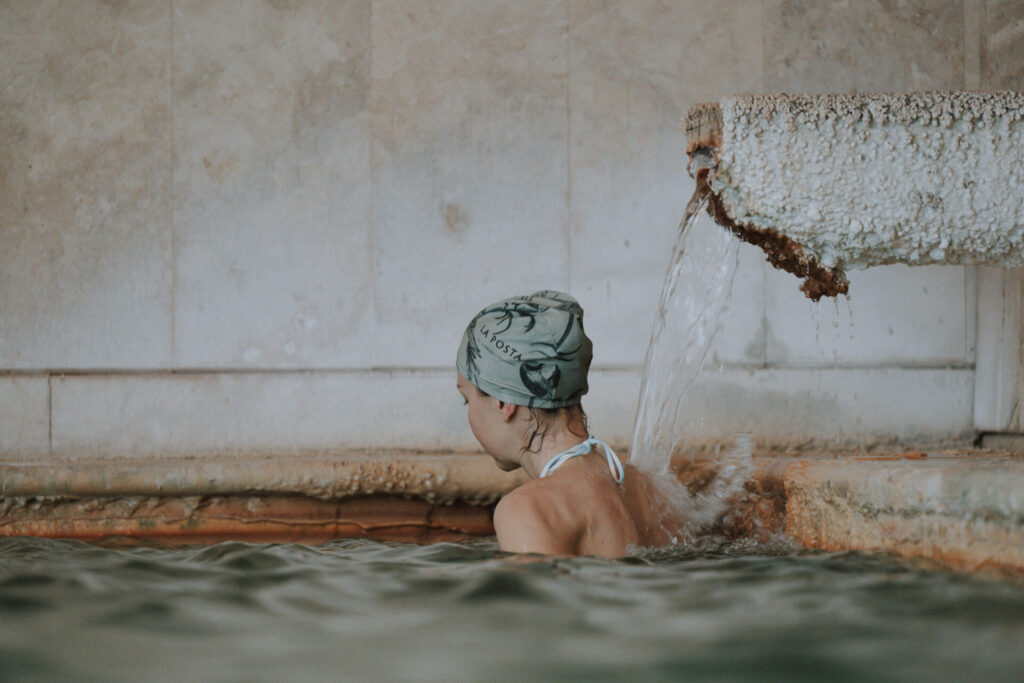 Ragazza sotto la cascata di acqua termale nella vasca interna